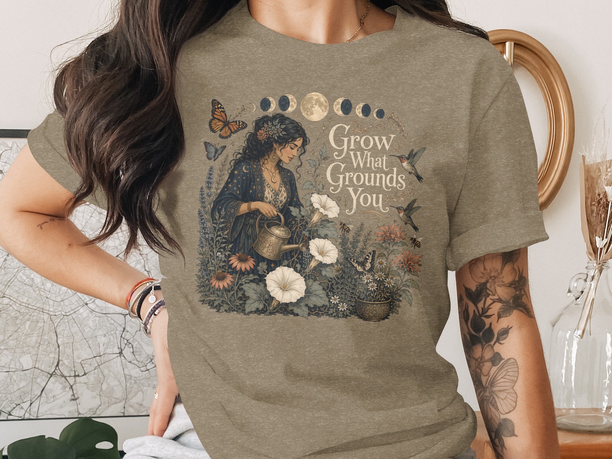 T-shirt graphic of woman watering plants with text "Grow What Grounds You."