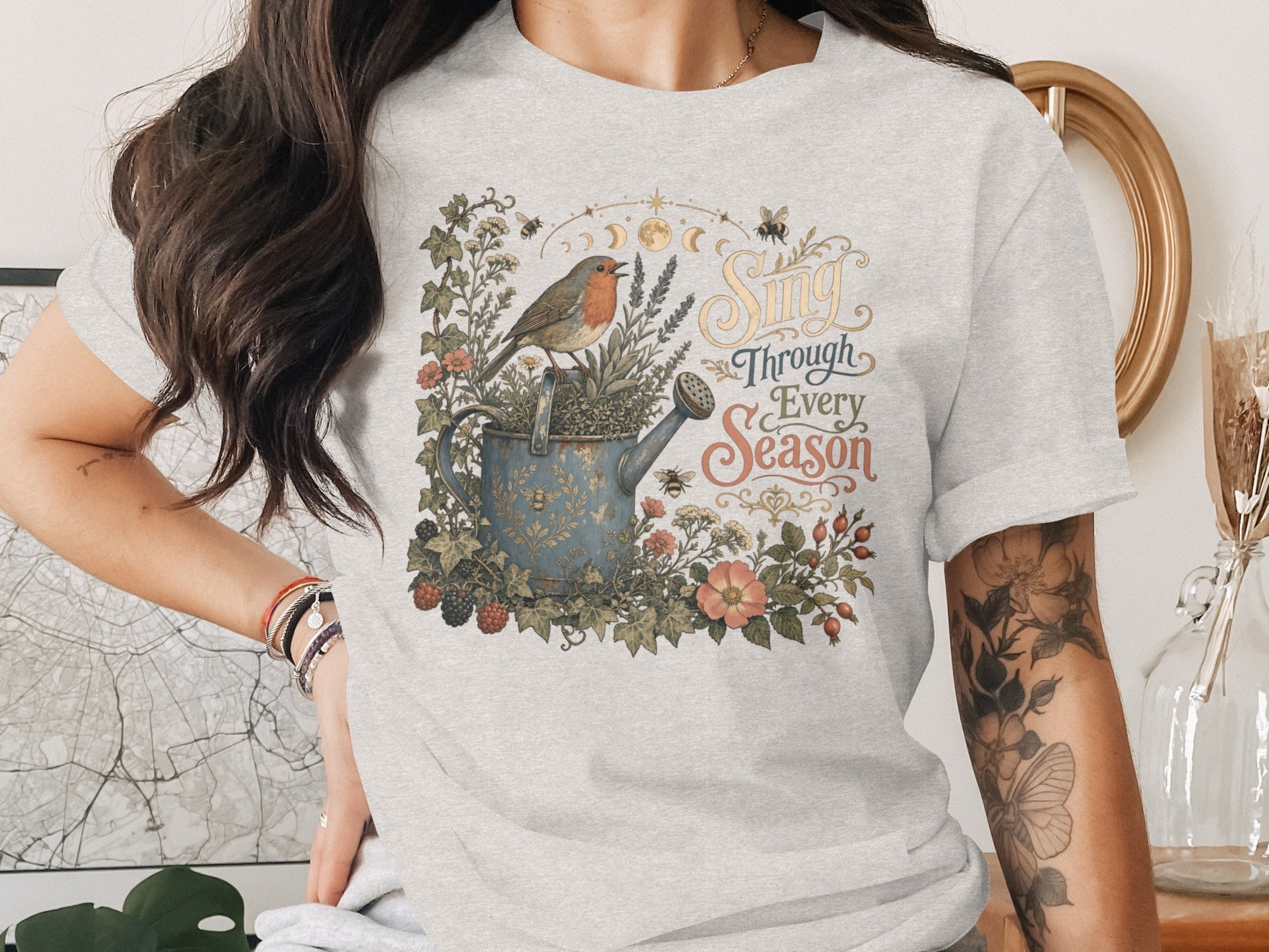 T-shirt graphic: robin on watering can with "Sing Through Every Season" text.