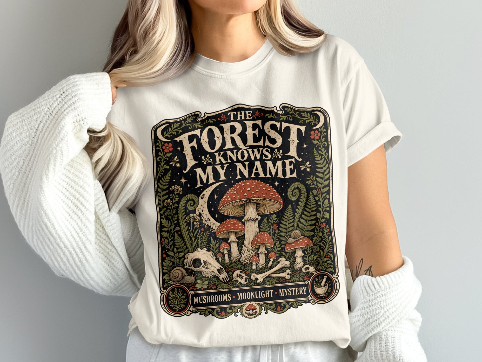 T-shirt with forest, mushrooms, skull, bones, moon, and text "The Forest Knows My Name".