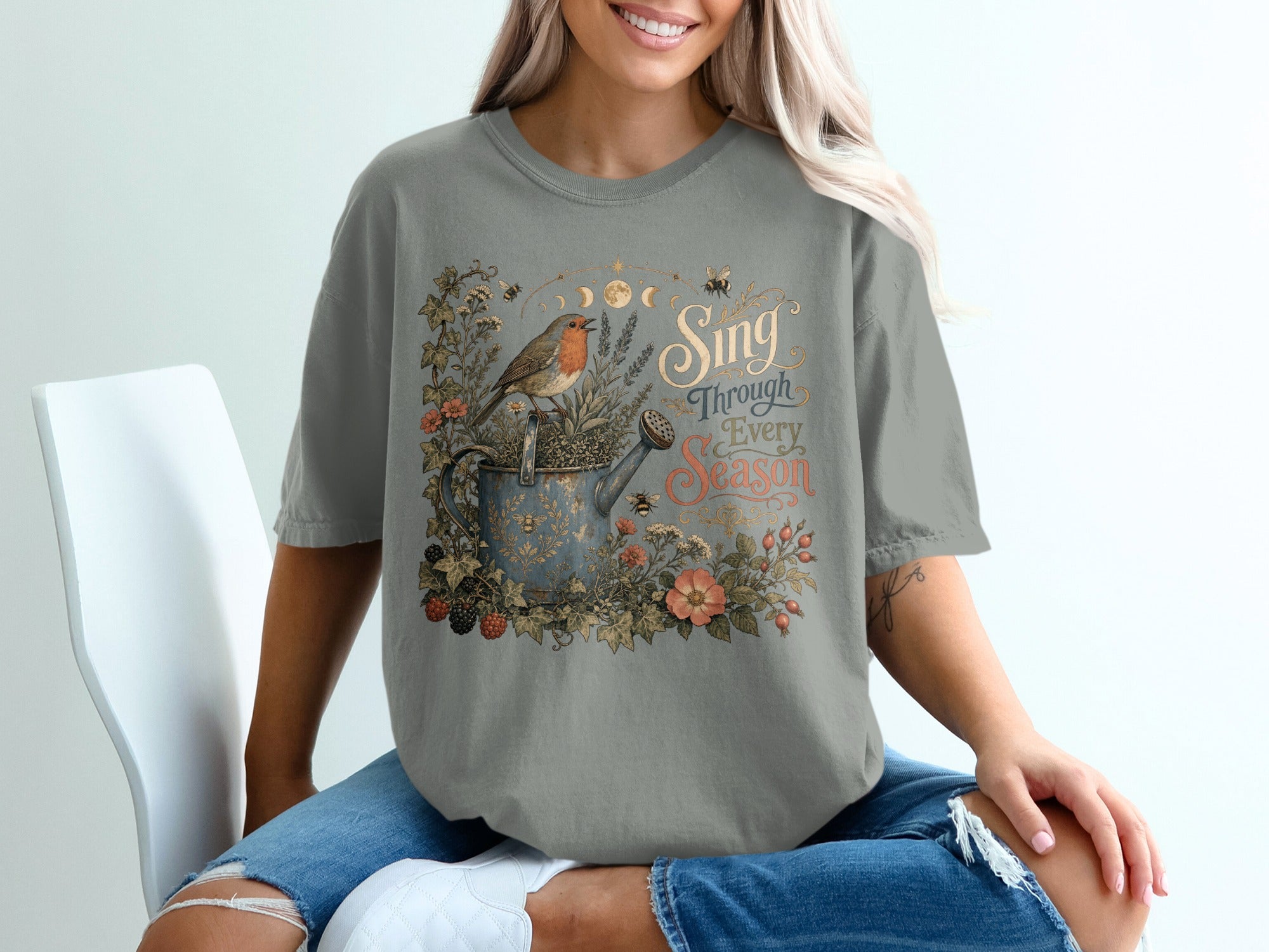 T-shirt with robin, watering can, flowers, and text "Sing Through Every Season".
