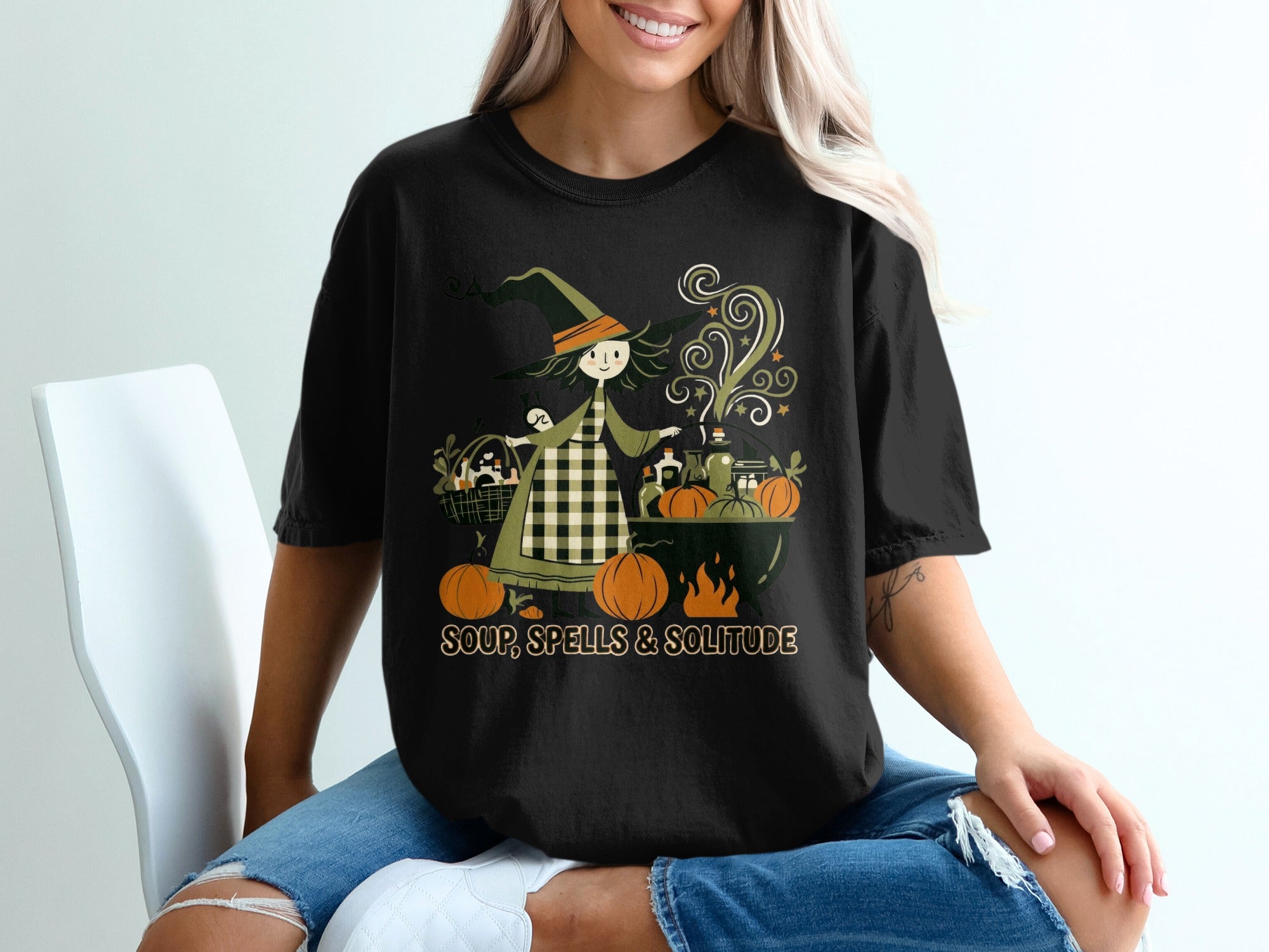 Black t-shirt with a witch stirring a cauldron, pumpkins, and text "SOUP, SPELLS & SOLITUDE".