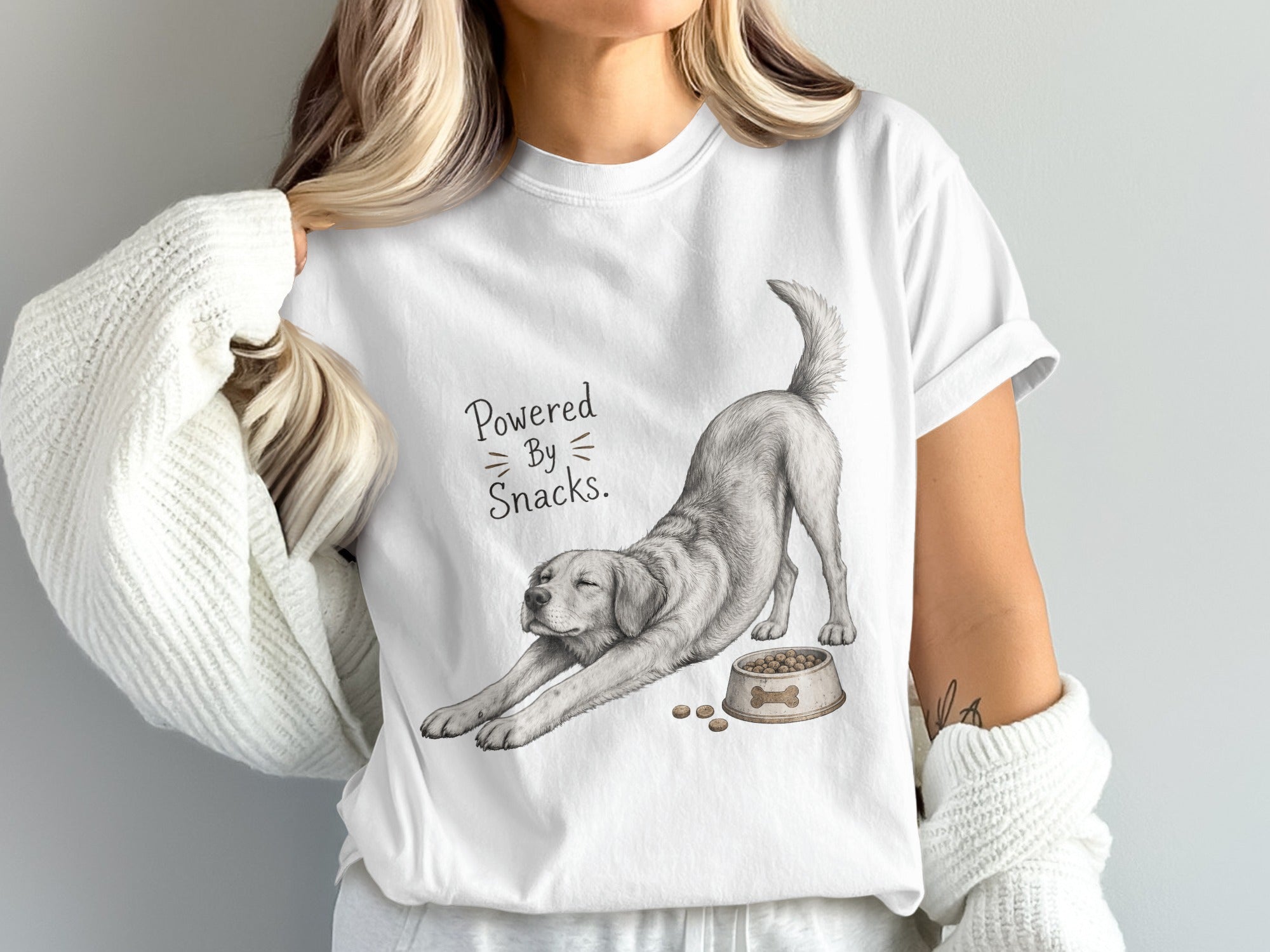 White t-shirt with a drawing of a dog stretching, dog bowl, and text "Powered By Snacks".