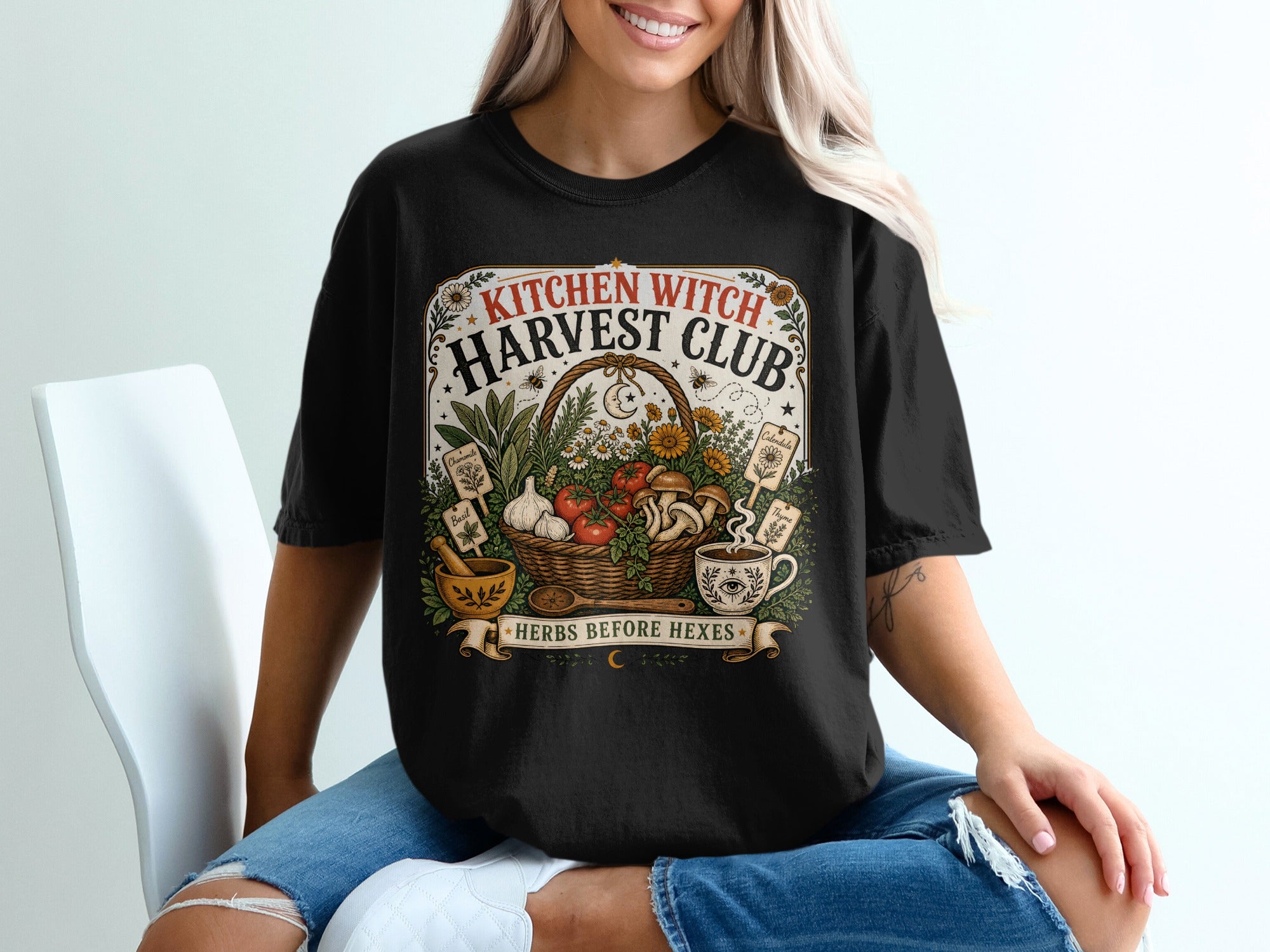 Black t-shirt with "Kitchen Witch Harvest Club Herbs Before Hexes" graphic.
