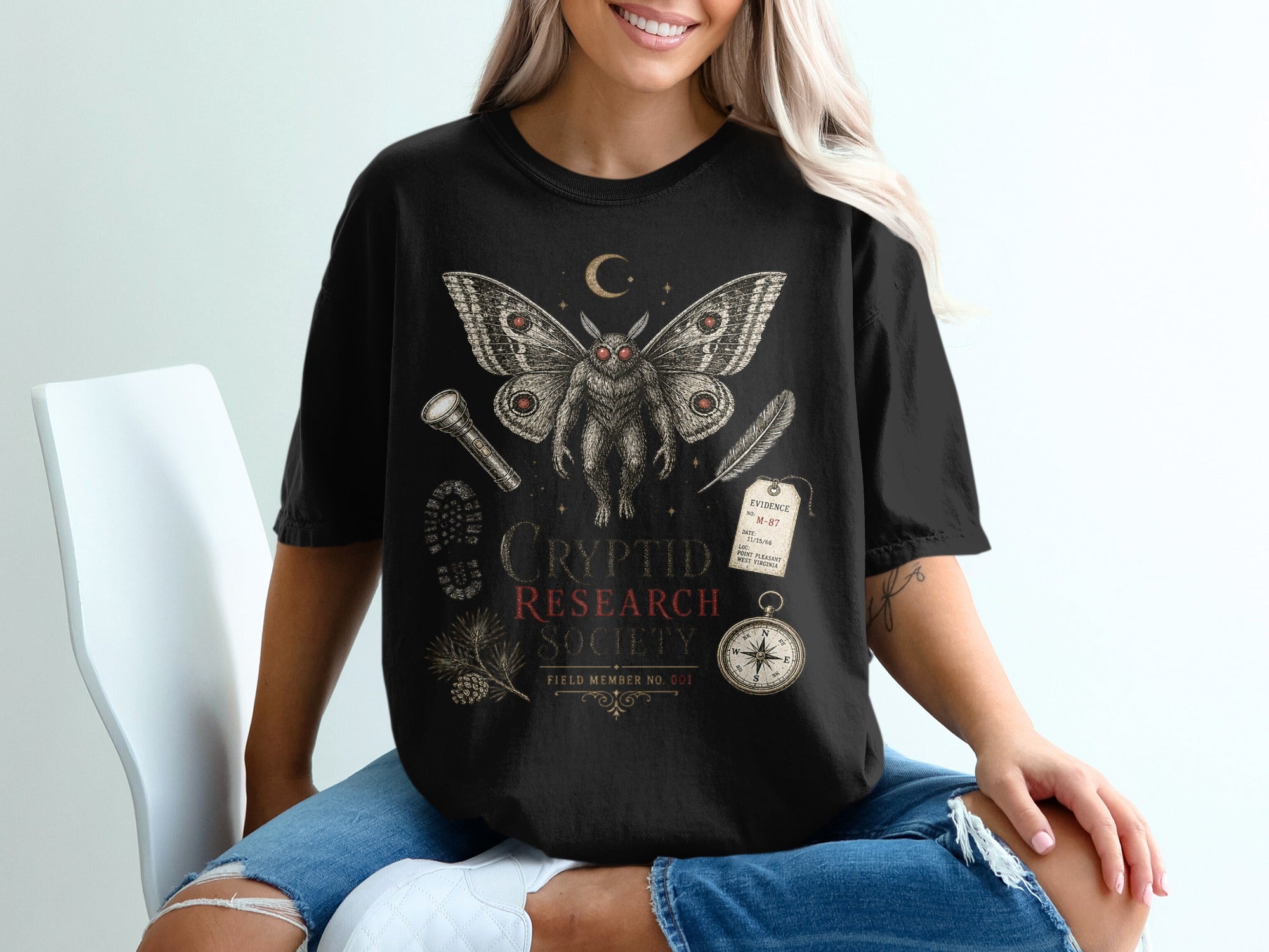 Black t-shirt with Cryptid Research Society graphic featuring a mothman, compass, and evidence tag.