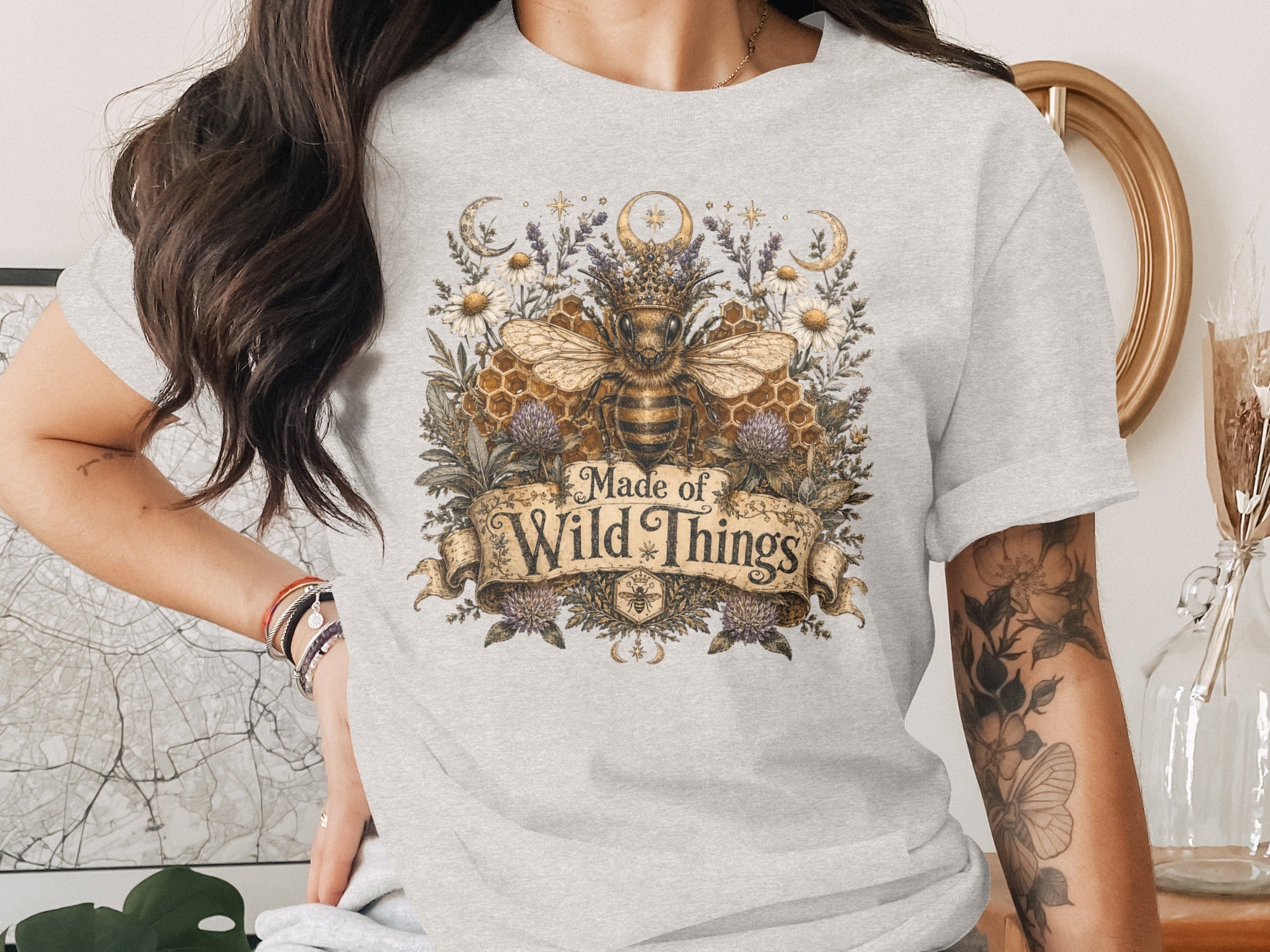 Bee with crown, honeycomb, flowers, moons, stars design on a grey t-shirt reads "Made of Wild Things".