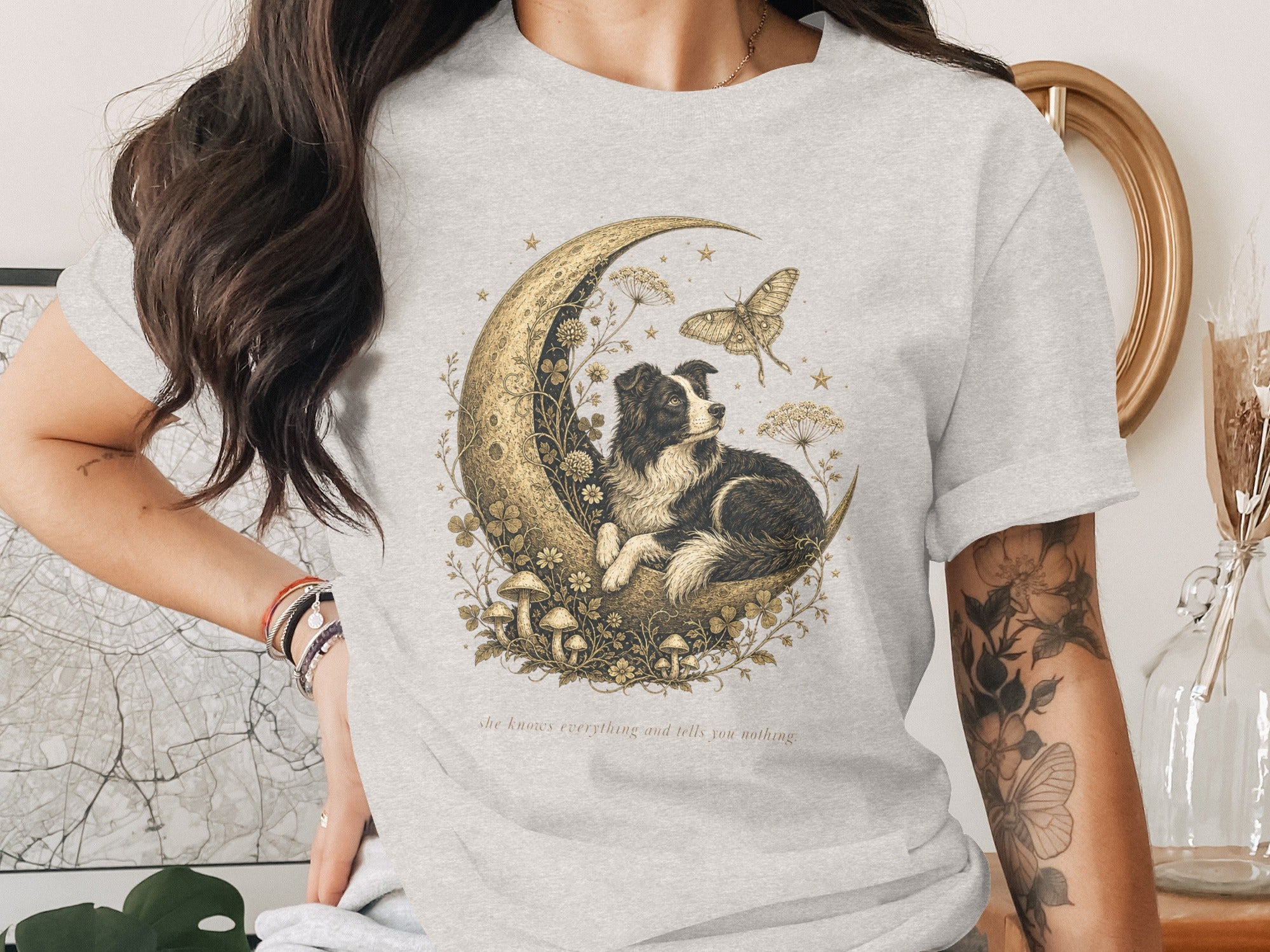 T-shirt graphic: Border collie on moon with butterfly, text "she knows everything and tells you nothing."