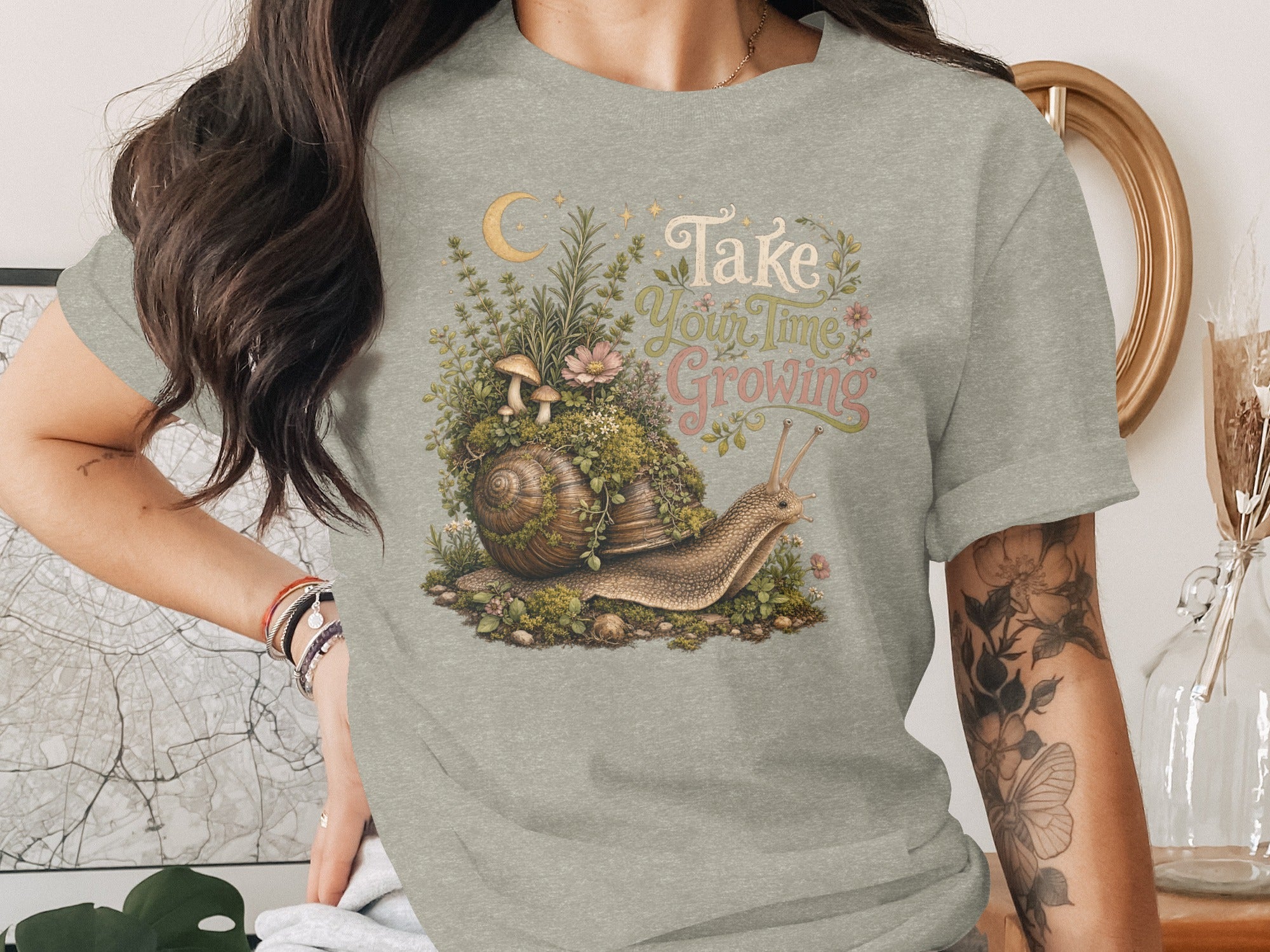 "Take Your Time Growing" text with a snail, mushrooms, and moon graphic on a t-shirt.