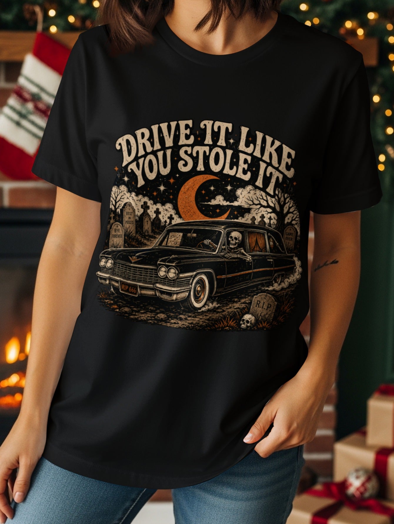 Black t-shirt graphic with skeleton driving a hearse through a graveyard under a crescent moon.