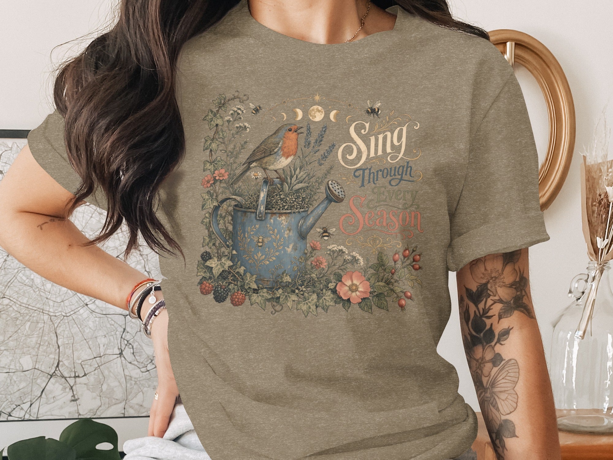 T-shirt graphic with robin on watering can and "Sing Through Every Season" text.