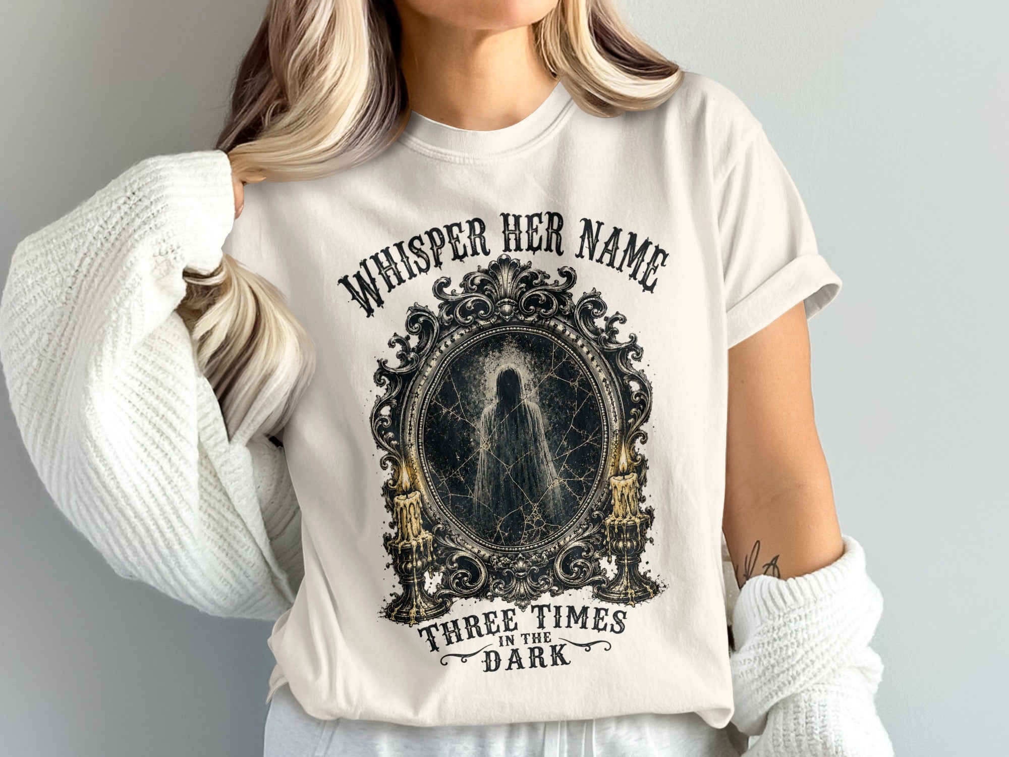 White t-shirt with "Whisper Her Name Three Times in the Dark" text and ghost graphic.