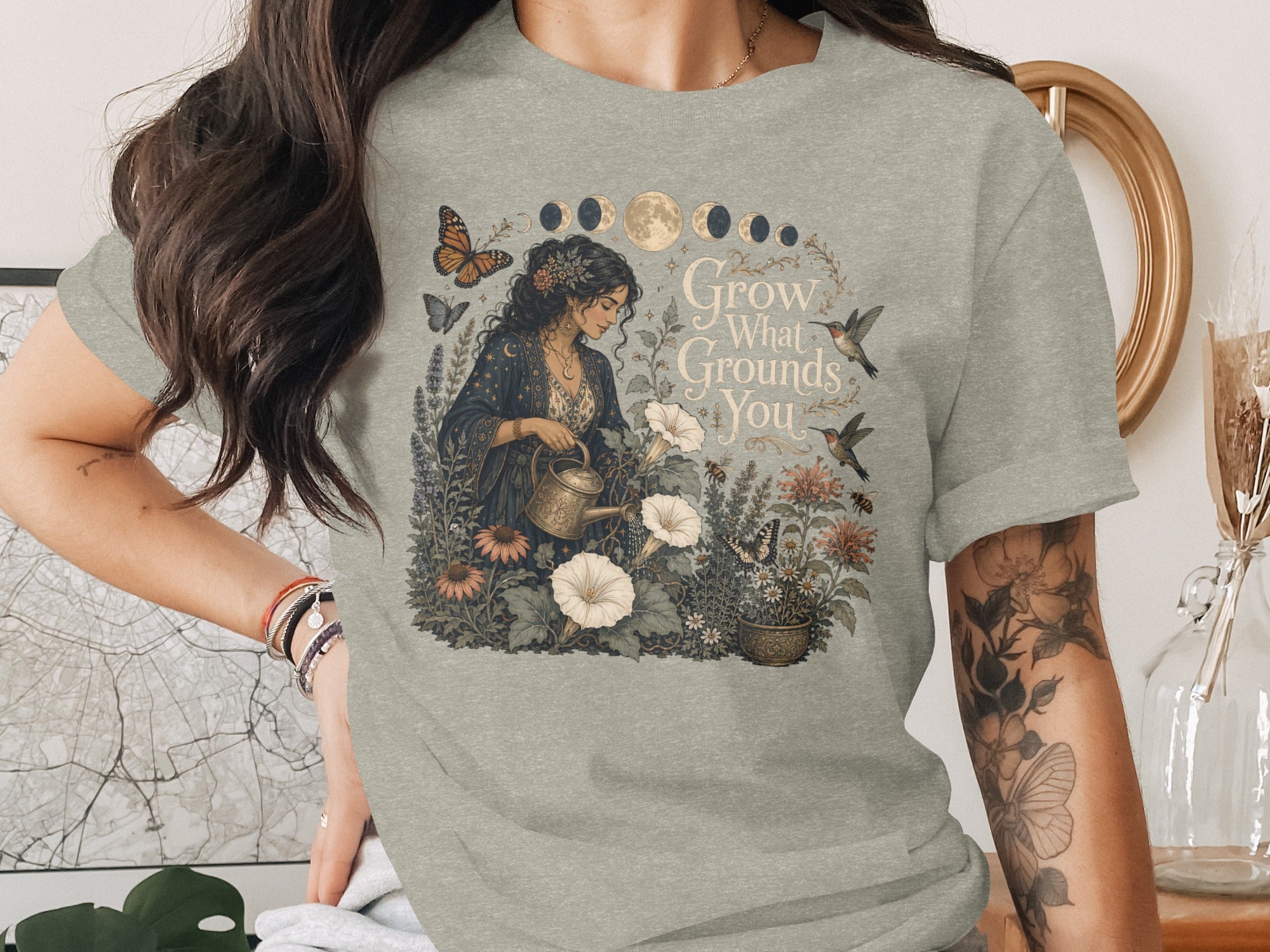 T-shirt graphic: Woman watering plants with text "Grow What Grounds You".