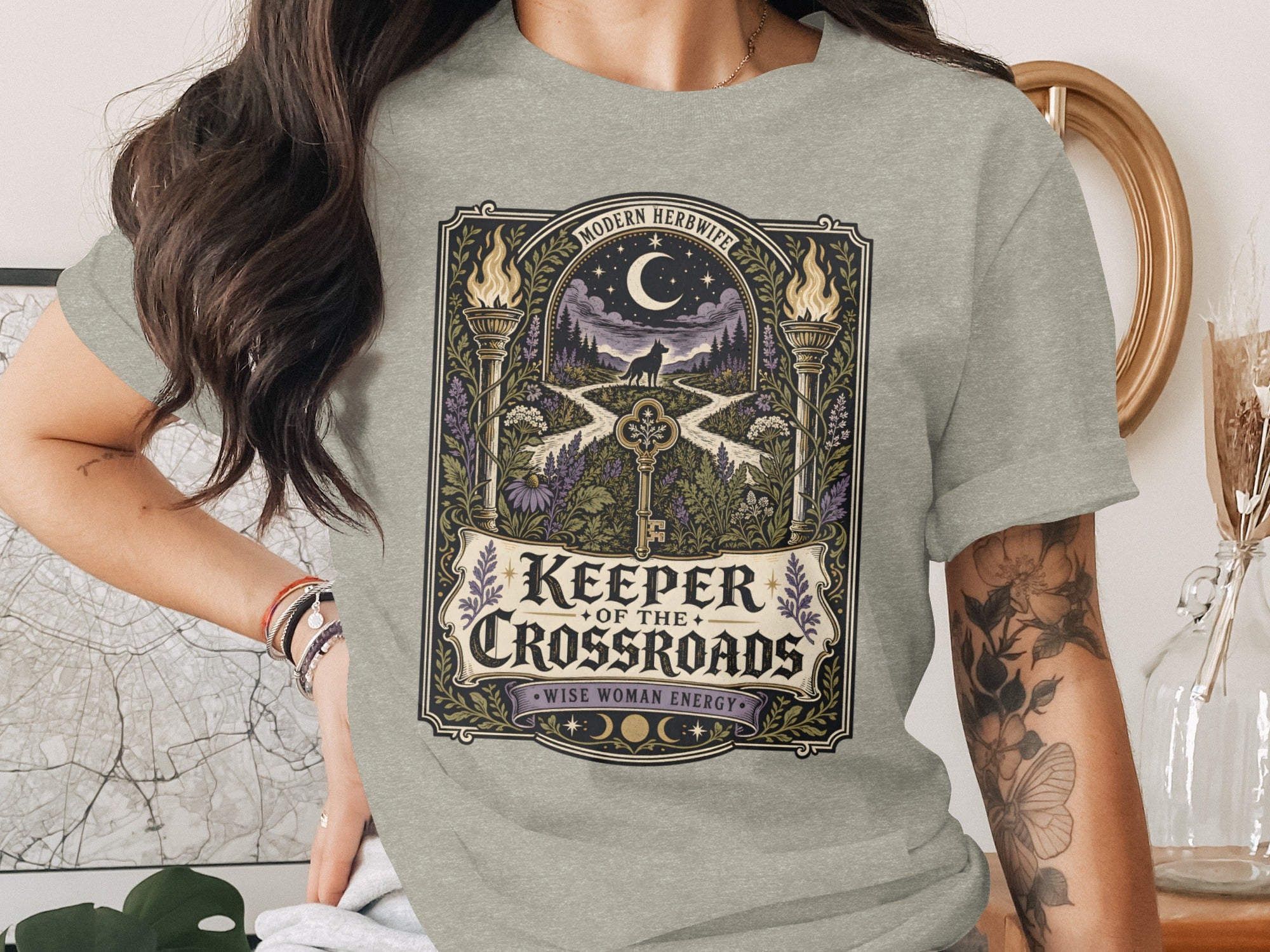 Gray t-shirt with "Keeper of the Crossroads Wise Woman Energy" text and forest scene.