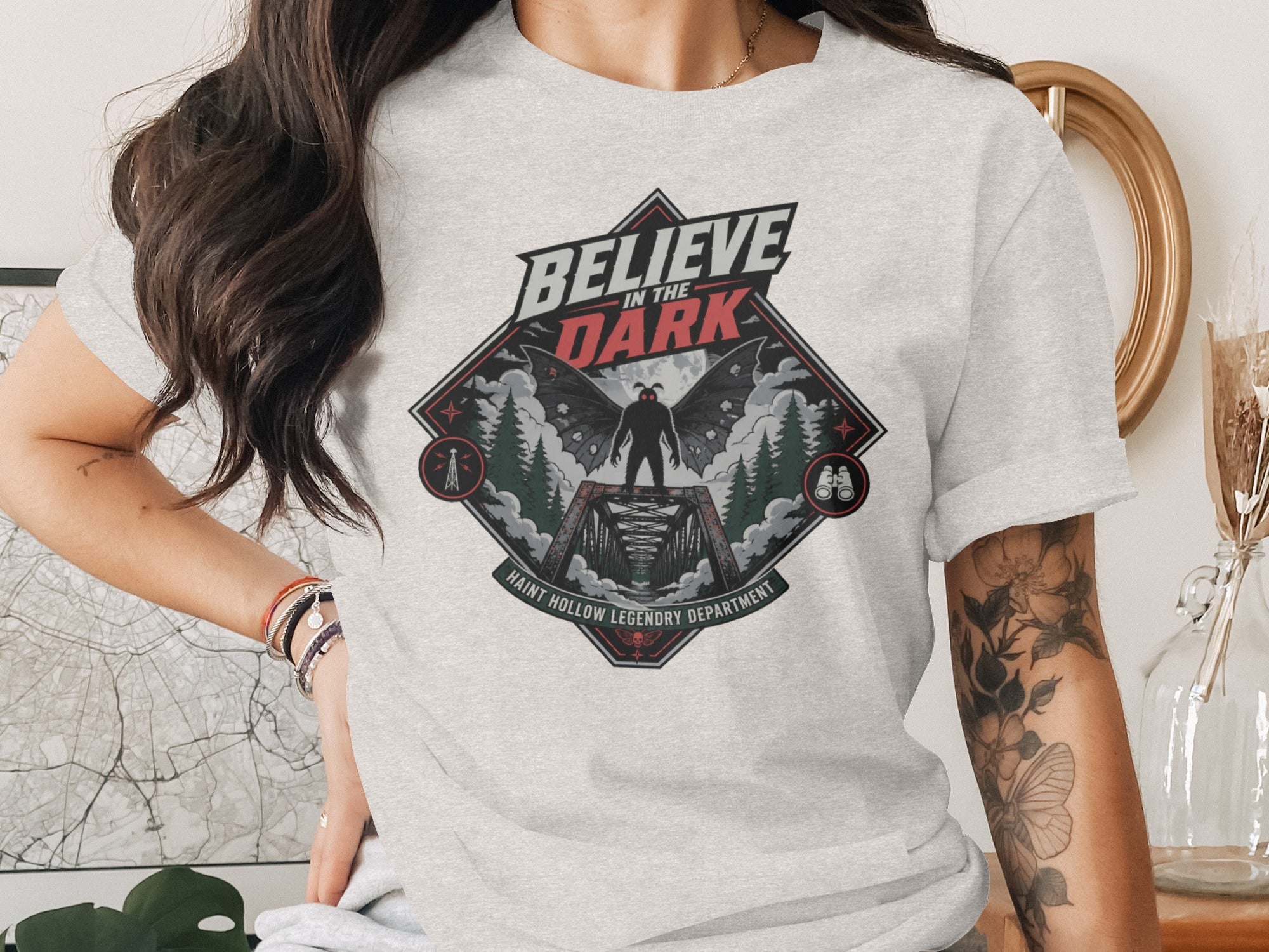Graphic tee with "Believe in the Dark" text, a winged creature on a bridge, and trees.