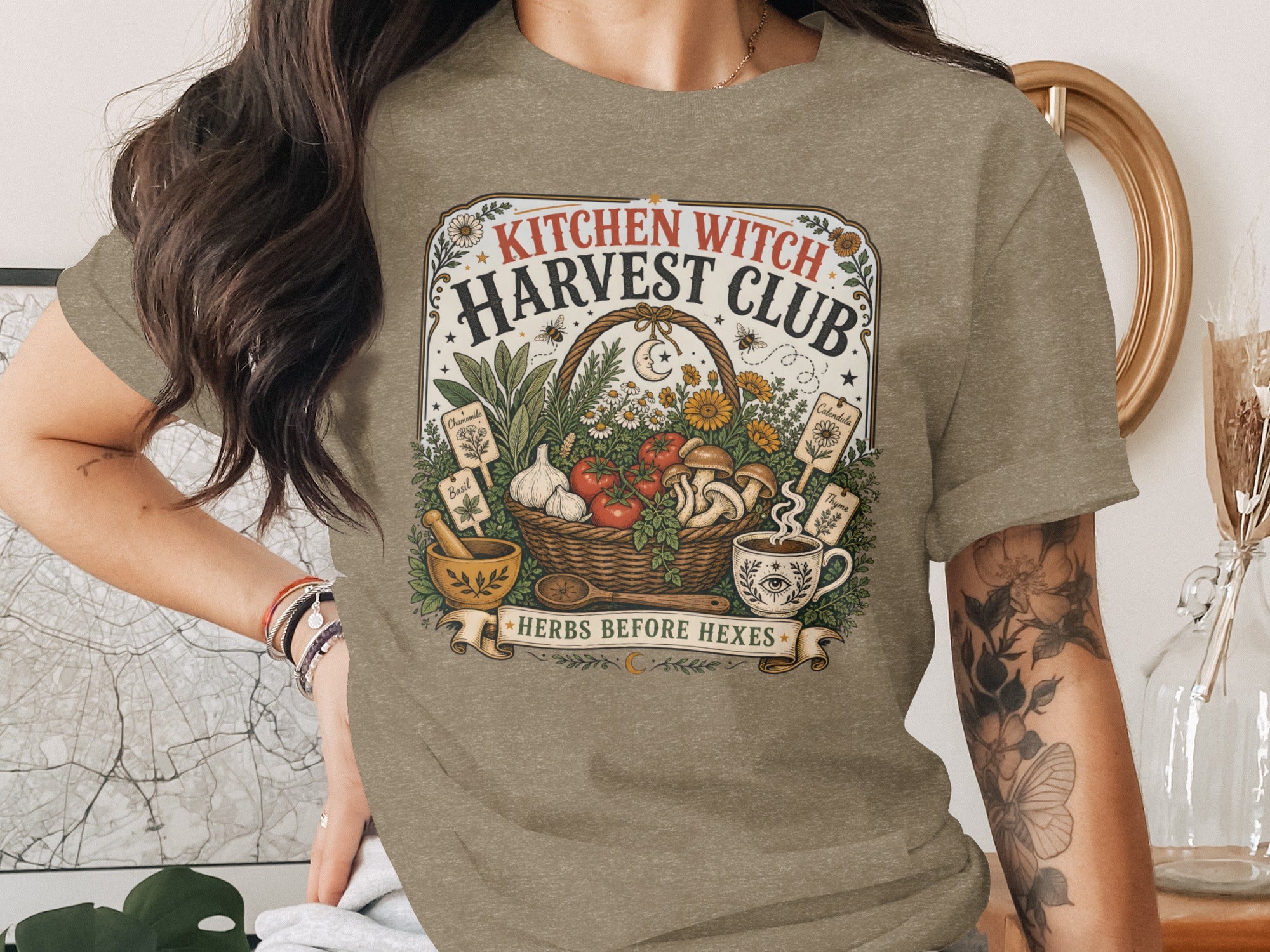 T-shirt with "KITCHEN WITCH HARVEST CLUB" and "HERBS BEFORE HEXES" text and harvest imagery.