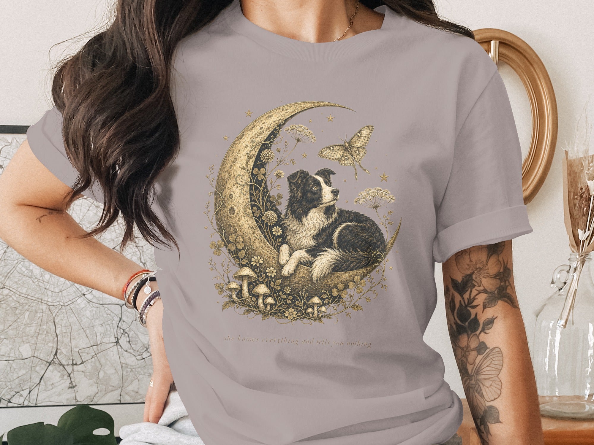 Border collie on crescent moon with butterfly, mushrooms, and text: "she knows everything and tells you nothing."
