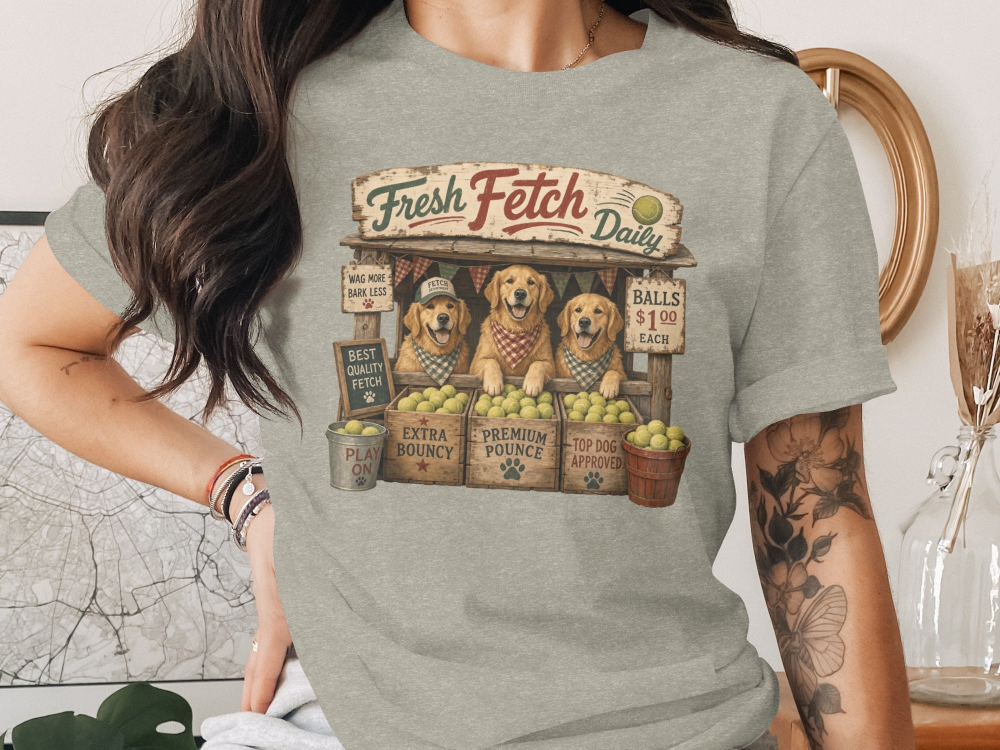 Three golden retrievers wearing bandanas at a "Fresh Fetch Daily" stand with tennis balls.