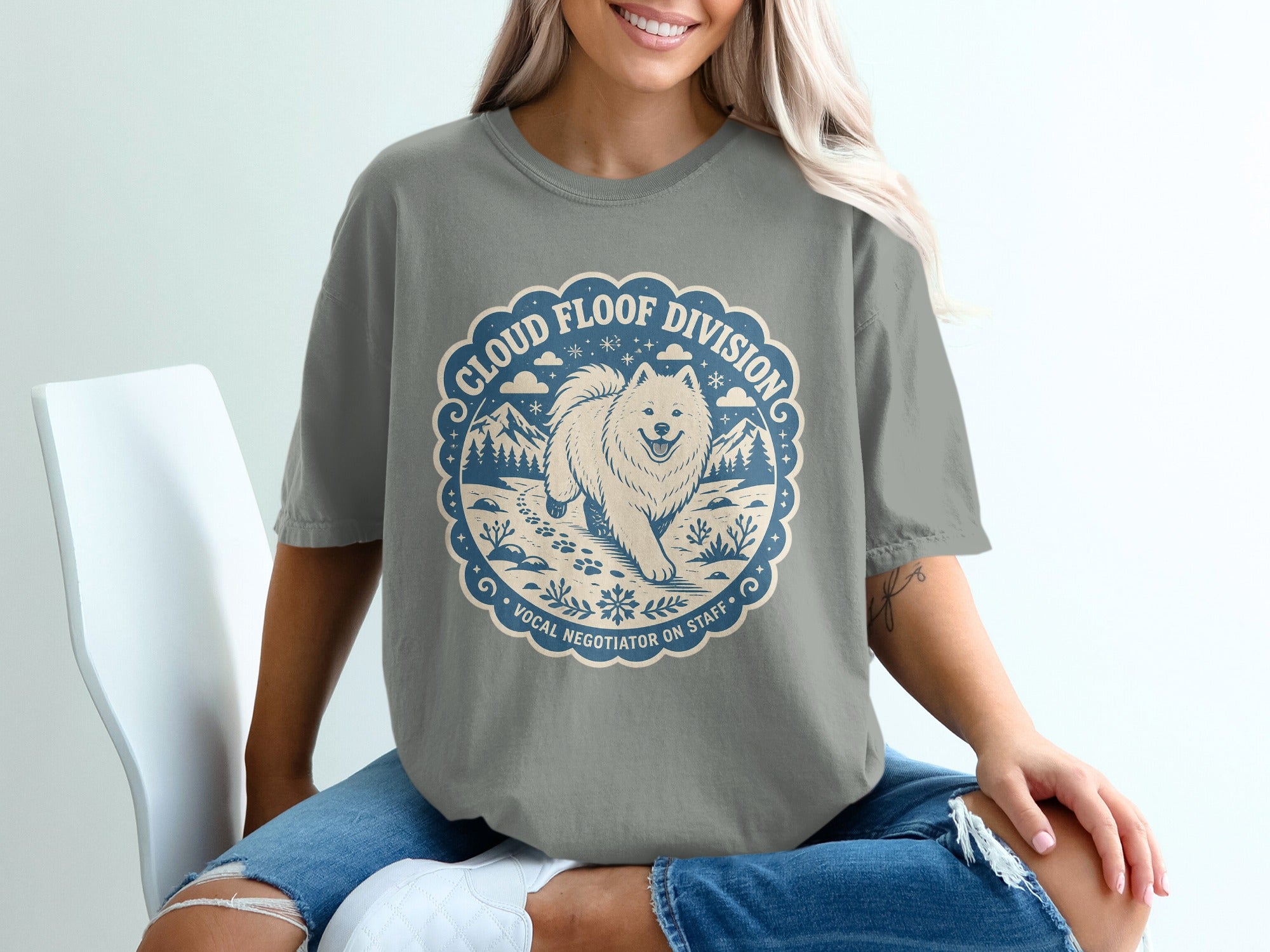 Gray t-shirt with a circular emblem featuring a fluffy dog, mountains, and text "Cloud Floof Division Vocal Negotiator On Staff".