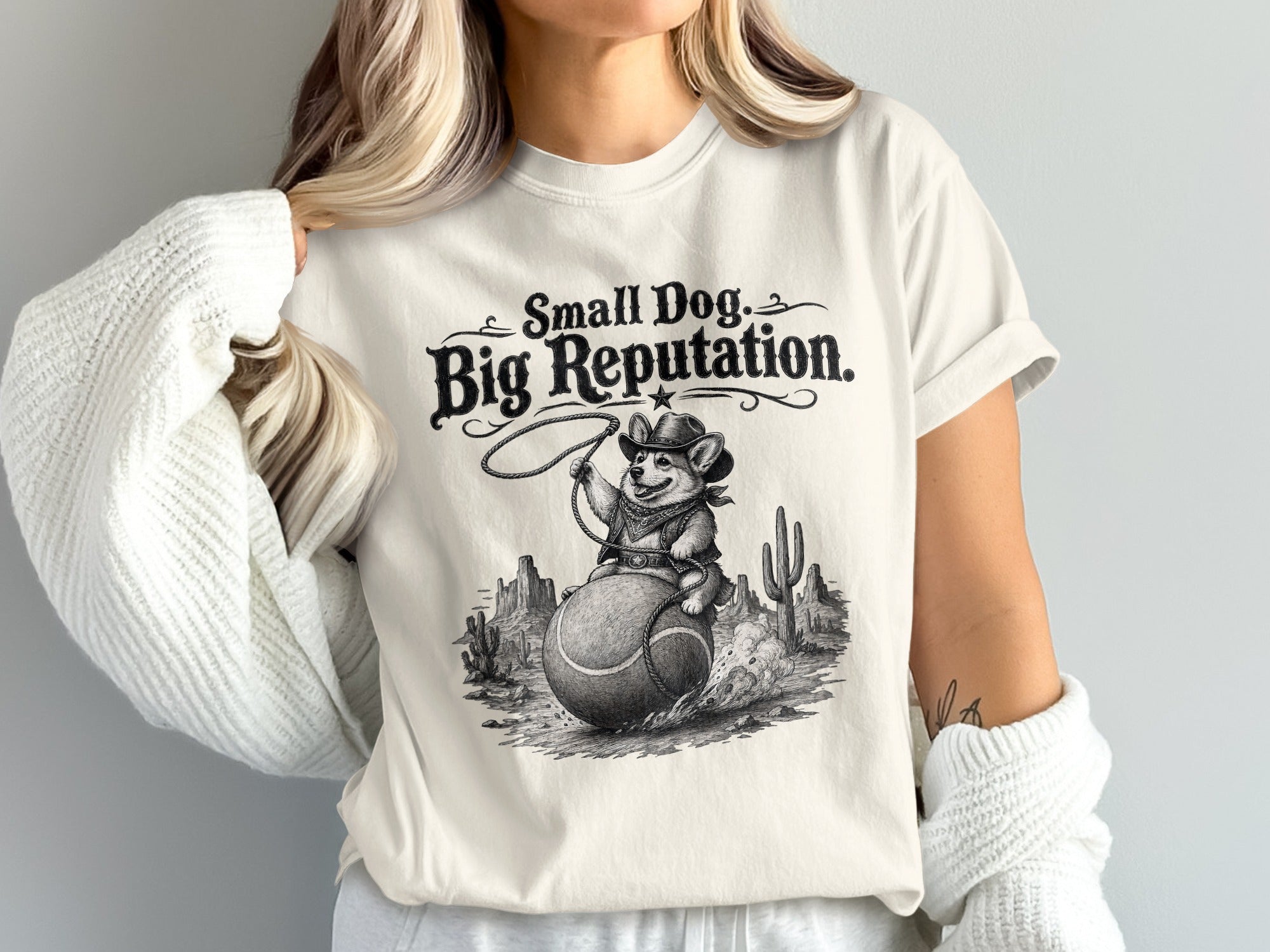 T-shirt with "Small Dog, Big Reputation" text and cowboy corgi riding a tennis ball in desert scene.