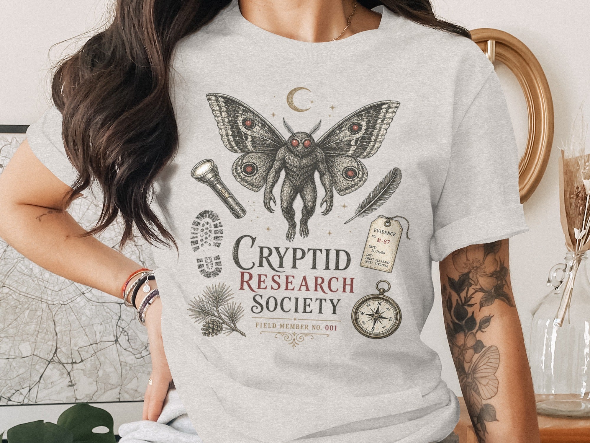 Cryptid Research Society t-shirt with mothman, evidence tag, compass, and footprint.