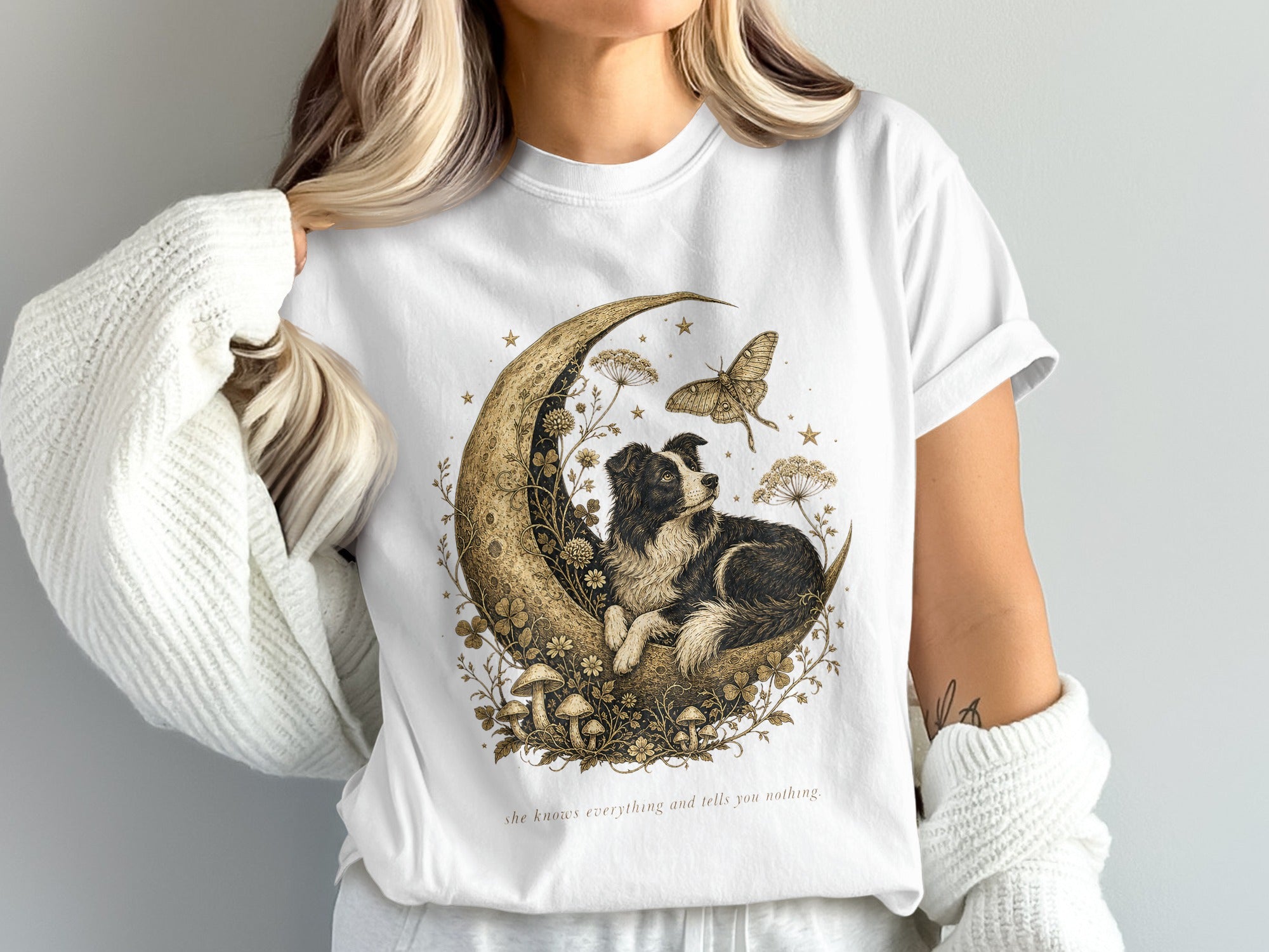 T-shirt with a dog on a crescent moon, butterfly, mushrooms, and text "she knows everything and tells you nothing."