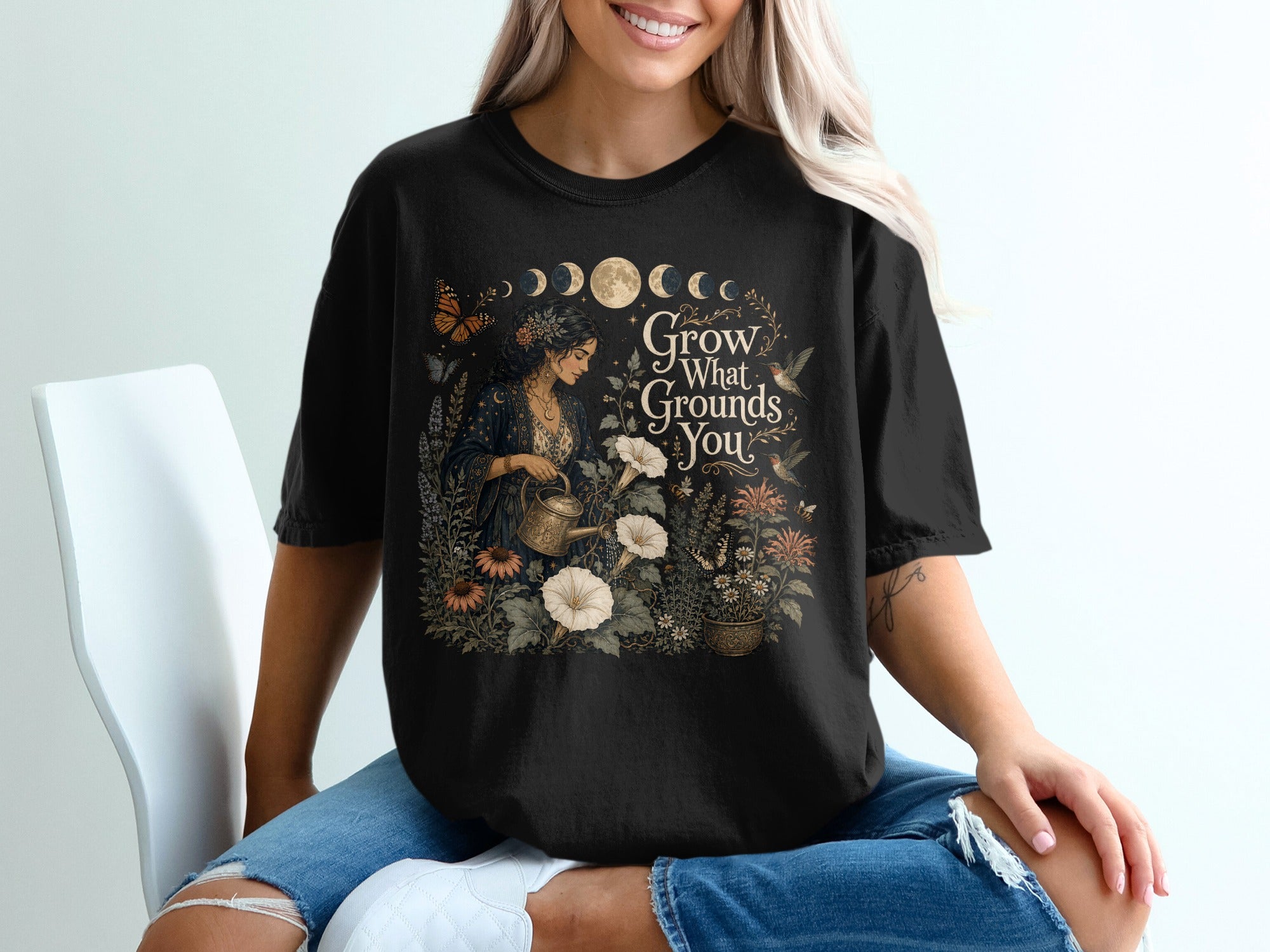 Black t-shirt with woman watering plants and "Grow What Grounds You" text.