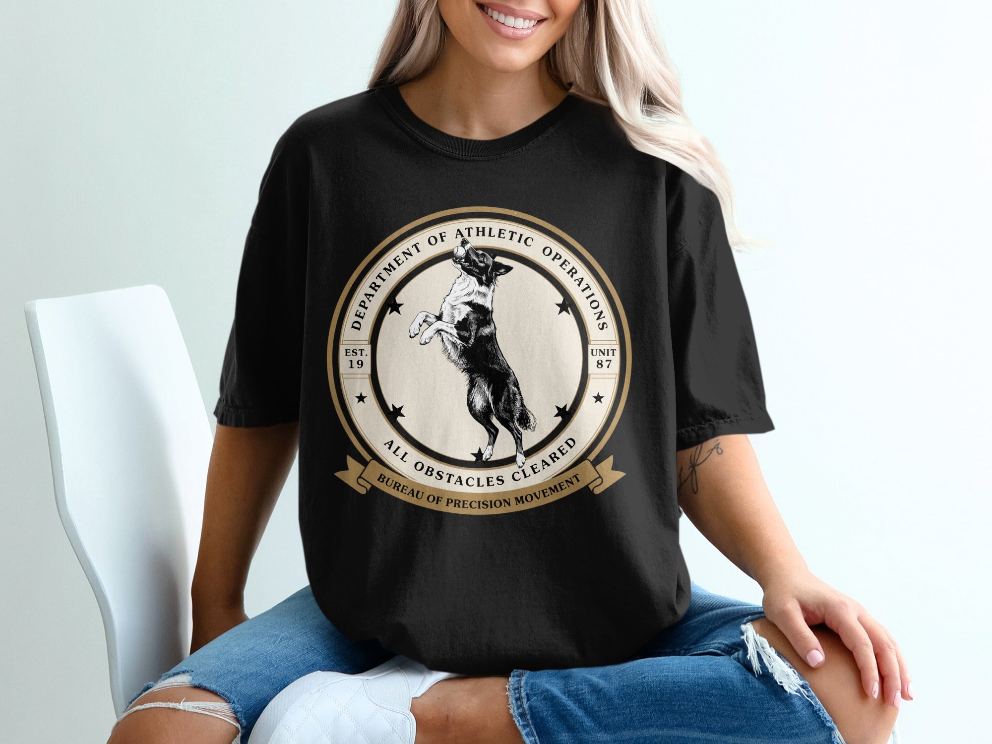 Black t-shirt with a circular graphic featuring a dog, "DEPARTMENT OF ATHLETIC OPERATIONS," and "ALL OBSTACLES CLEARED."