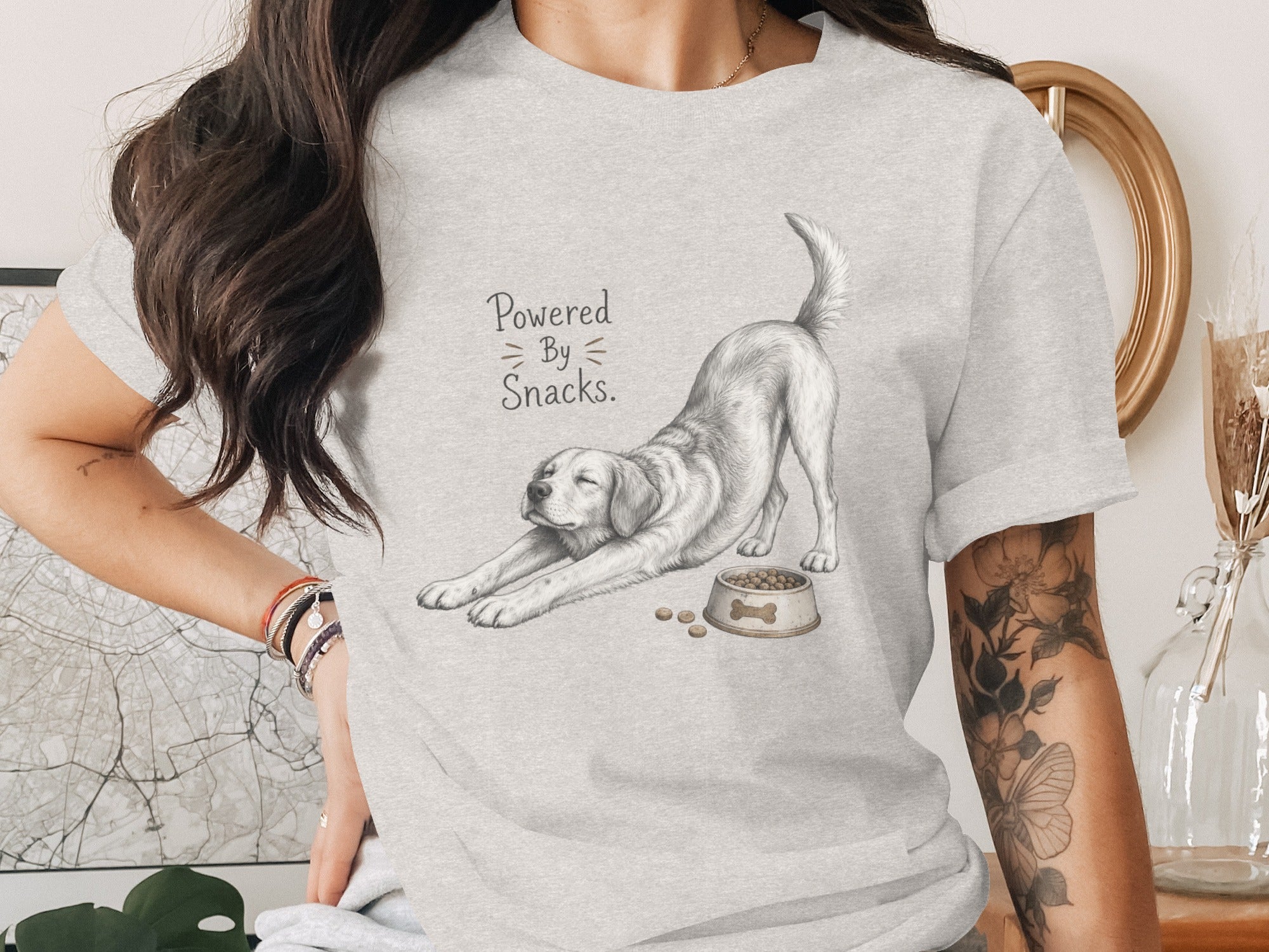 Gray t-shirt with a drawing of a dog stretching by a bowl of food, text reads "Powered By Snacks."