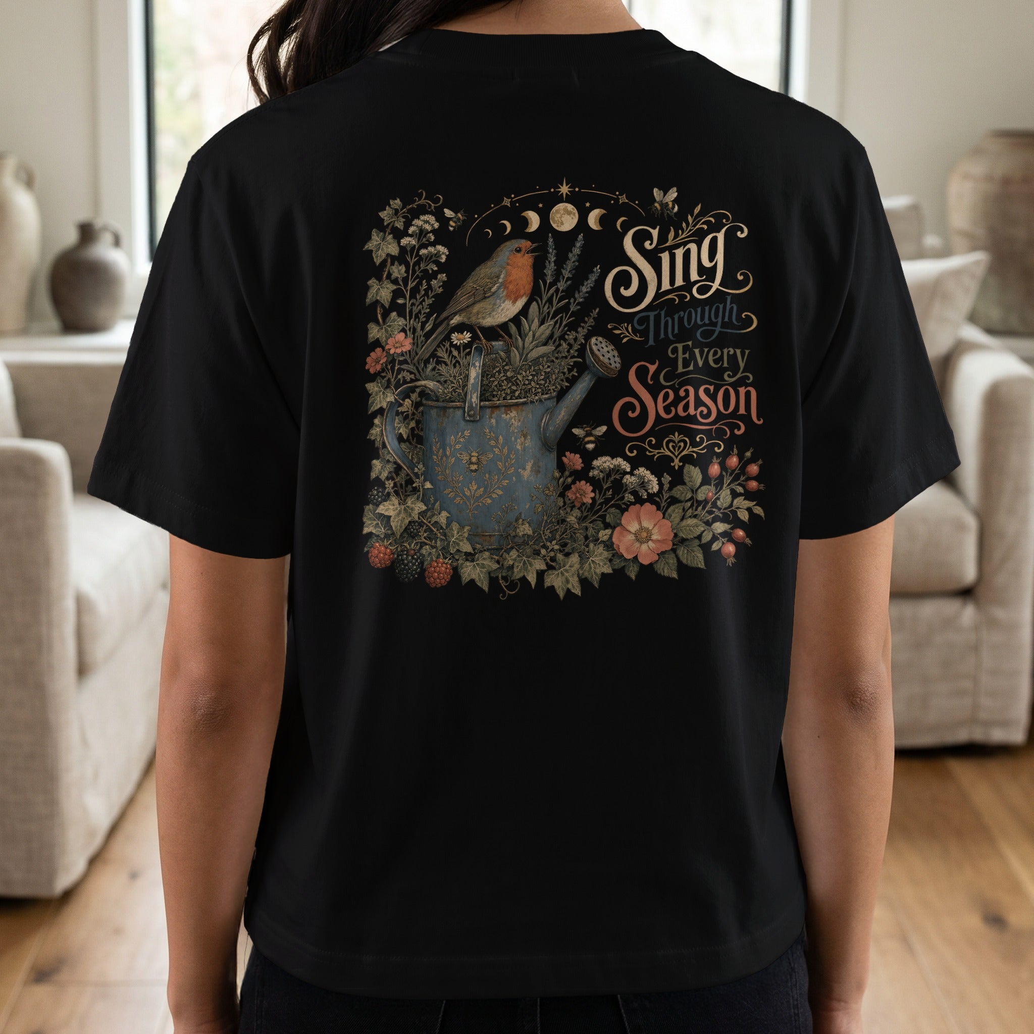 Black t-shirt with a robin on a watering can, surrounded by flowers and text.